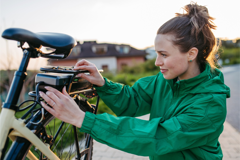 Rowerzystka montująca baterię na bagażniku roweru elektrycznego