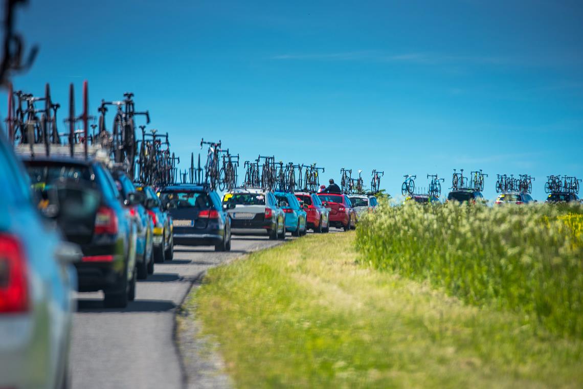 Długa kolejka samochodów z licznymi rowerami dla uczestników Tour de France.